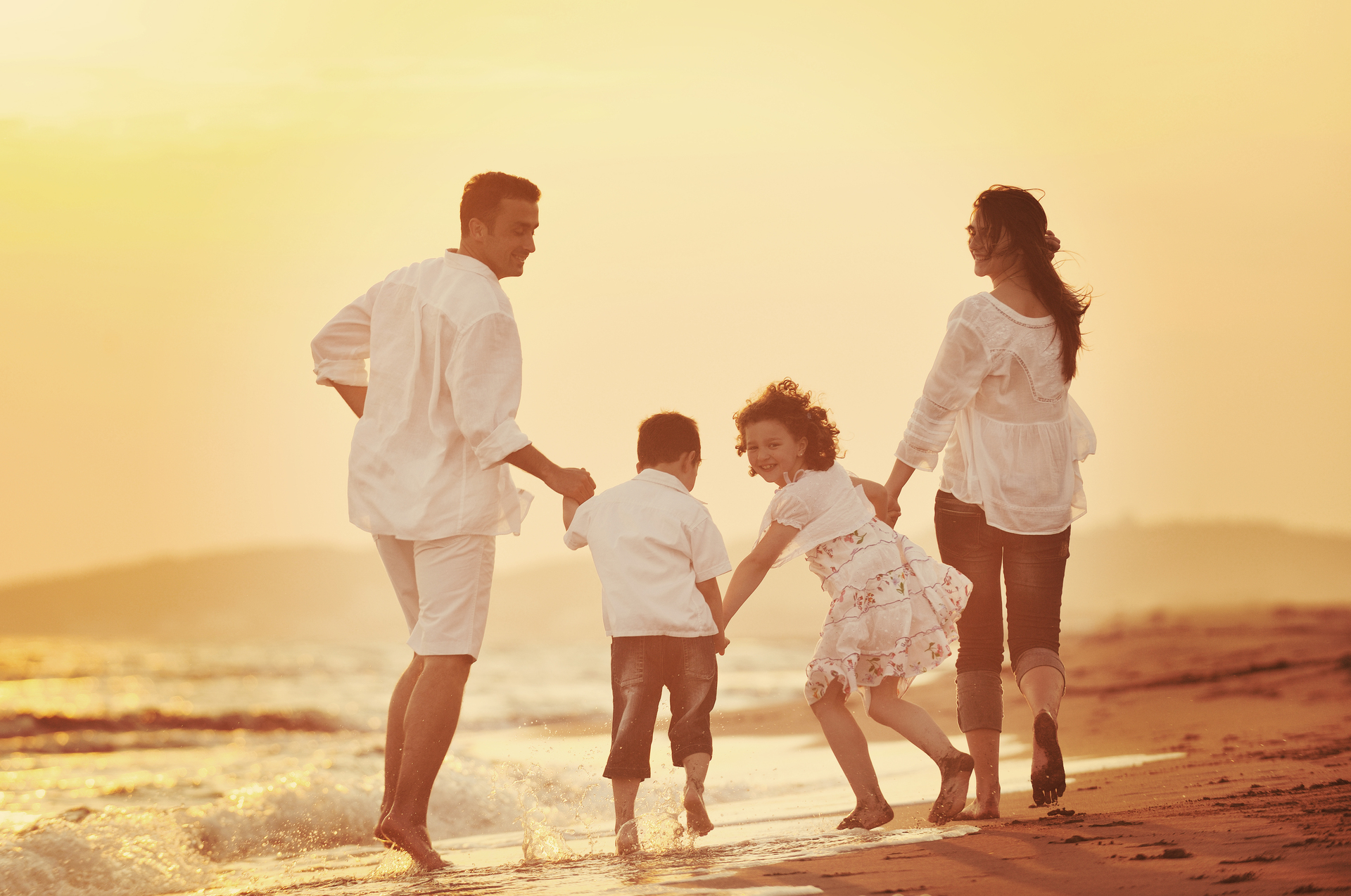 Na zdjęciu widoczna jest tradycyjna rodzina podczas spaceru po plaży. W skład rodziny wchodzą rodzice i dwoje dzieci, którzy trzymają się za ręce i uśmiechają się do siebie. W tle widać piękne, malownicze krajobrazy, co dodaje uroku temu rodzinnemu spacerowi. Taki obrazek przypomina nam o wartościach rodzinnych i pokazuje, jak ważne jest spędzanie czasu razem, zwłaszcza na łonie natury.