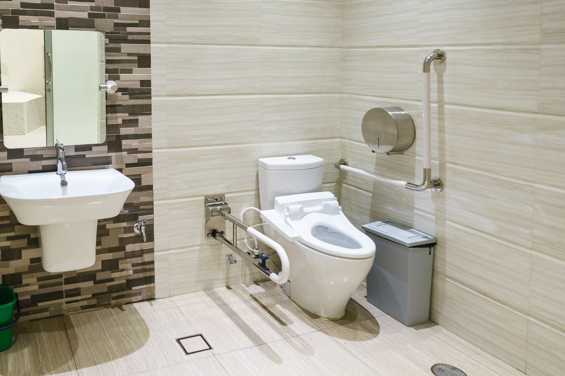 Na obrazku widoczna jest funkcjonalna łazienka stworzona z myślą o osobach niepełnosprawnych. Wnętrze charakteryzuje się przestronnością oraz liczba udogodnień, które ułatwiają codzienne czynności. W łazience znajduje się m.in. specjalnie zaprojektowany podjazd, poręcze, dostępny prysznic na poziomie podłogi oraz odpowiednio umieszczone uchwyty, które zapewniają bezpieczeństwo i wygodę użytkowania dla osób o ograniczonej mobilności