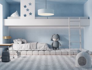 Przedstawione zdjęcie ukazuje uroczy pokój dziecięcy w odcieniach niebieskiego. Na ścianach widoczne są jasnoniebieskie tapety w biało-niebieskie paski, które dodają pomieszczeniu lekkości i świeżości. Na podłodze położony jest miękki dywan w kolorze błękitnym, a na łóżku znajduje się kolorowa pościel w motywy morskie. Przestrzeń ta została urządzona w sposób stonowany, ale jednocześnie ciepły i przytulny.