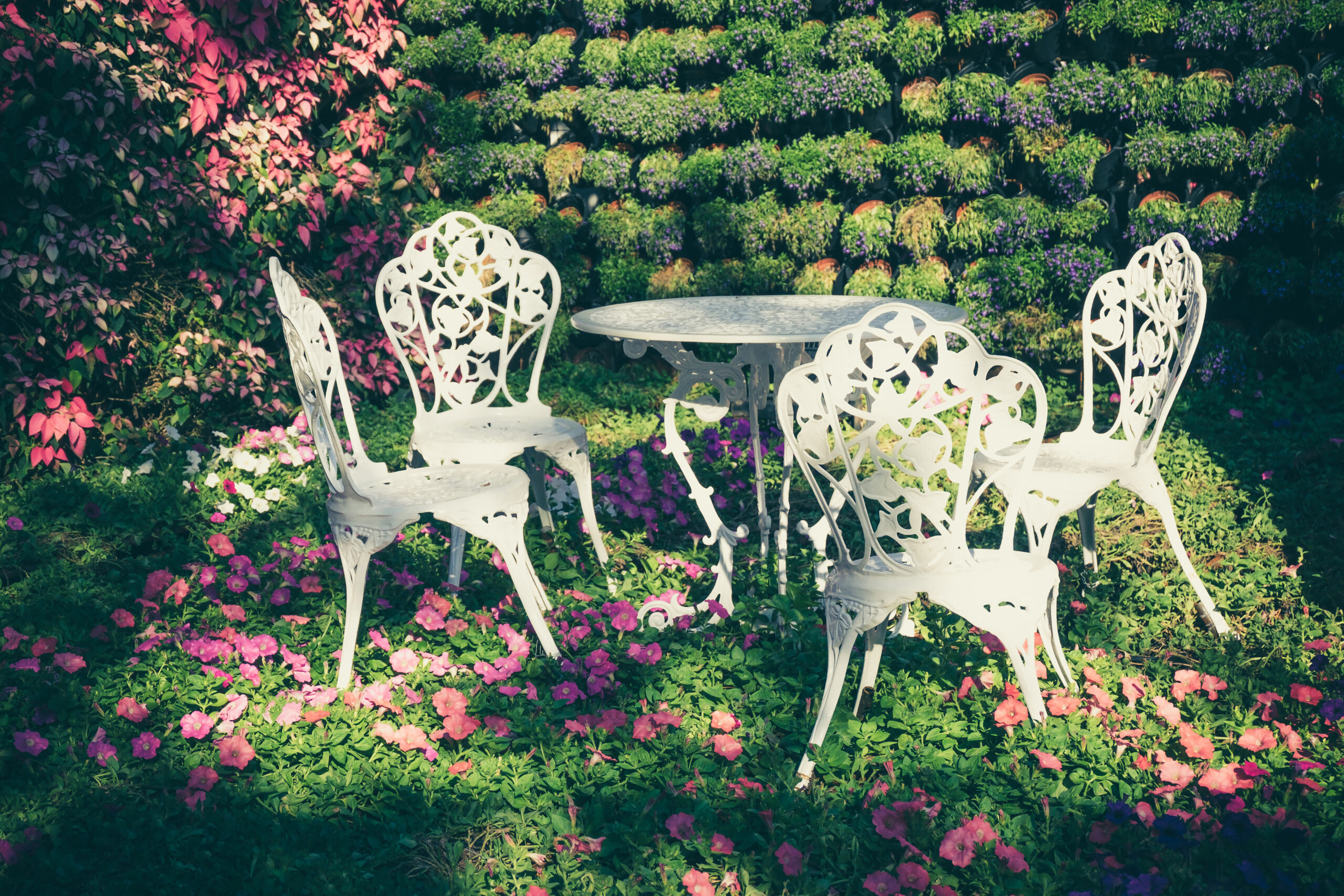 Białe meble w stylu vintage dodają subtelności i lekkości temu ogrodowi, tworząc przytulne miejsce do odpoczynku i relaksu w pięknej scenerii