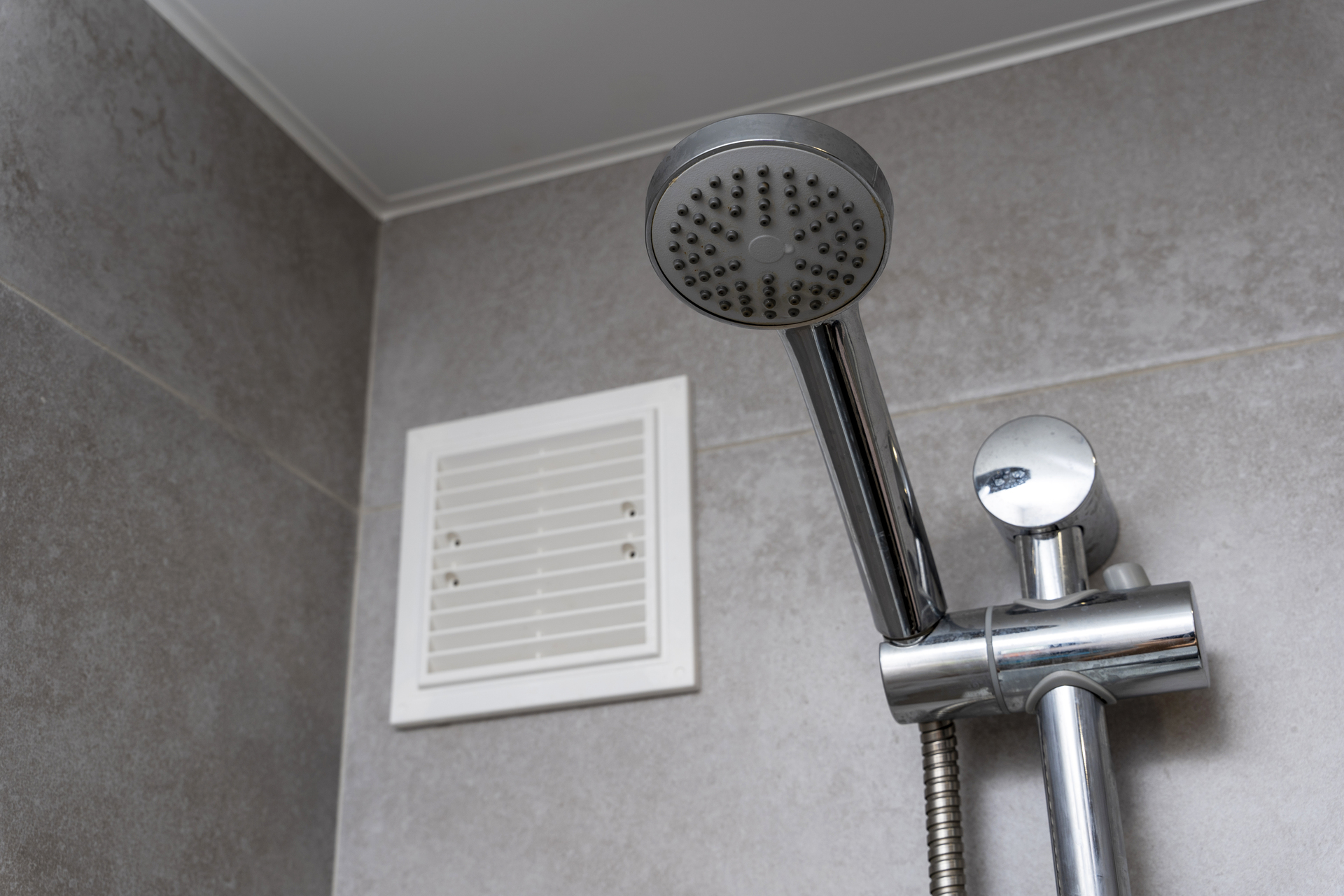 Na obrazku widoczny jest wentylator umieszczony nad prysznicem w łazience, zapewniający skuteczną eliminację pary wodnej i wilgoci. Jego precyzyjne umiejscowienie pozwala na skuteczne odprowadzanie powstałej pary, co pomaga utrzymać środowisko łazienki suche i świeże. Ten obrazek ukazuje praktyczne zastosowanie wentylatora w łazience, dbając o zapobieganie powstawaniu pleśni i utrzymanie optymalnej kondycji pomieszczenia