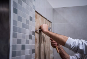 Obrazek przedstawia mężczyznę, który pełen entuzjazmu przystępuje do remontu łazienki. W rękach trzyma narzędzia i ma na sobie pracowniczy strój, gotowy do wyzwania. W tle widać rozpoczęte prace, co świadczy o determinacji i zaangażowaniu w przemianę tego pomieszczenia