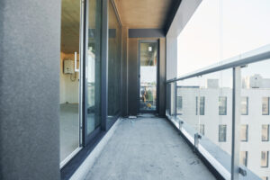 Obrazek ukazuje energiczną scenę remontu balkonu, gdzie specjaliści pracują z zaangażowaniem i precyzją. Wokół nich rozmieszczone są narzędzia, materiały budowlane i elementy wykończeniowe, świadczące o intensywności prac i dbałości o detale. Przemienione i odświeżone wnętrze balkonu wskazuje na stworzenie funkcjonalnego i estetycznego miejsca odpoczynku i relaksu