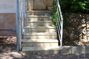 Na obrazku widoczne są stare zewnętrzne schody, które wymagają gruntownego remontu. Ich powierzchnia jest wytarta, a poszczególne stopnie są uszkodzone. Ta obrazkowa scena ukazuje potrzebę odnowienia tych schodów i przywrócenia im estetycznego wyglądu oraz bezpiecznej kondycji